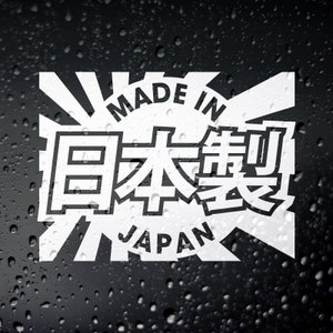 May include: White vinyl sticker featuring a rising sun design and the text "Made in Japan" within a circle. The Japanese characters for "Japan" are also incorporated into the design.
