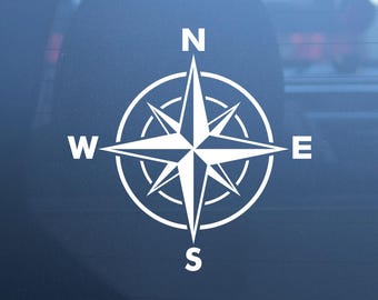 May include: A white vinyl decal featuring a compass rose design with four cardinal points marked by the letters N, S, E, and W. The graphic consists of a central star shape enclosed within a circular border, displaying clear, sharp lines.
