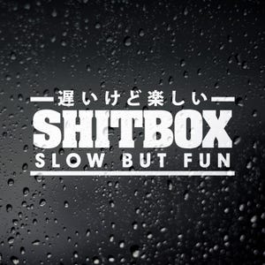 May include: White sticker with Japanese text and the words "Shitbox Slow But Fun" on a black background with water droplets.