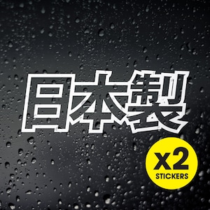 May include: Two white vinyl stickers featuring the Japanese characters for "Japan" and "Drift" in a bold, blocky font. The stickers are on a black background with water droplets. The text "x2 Stickers" is on a yellow circle.