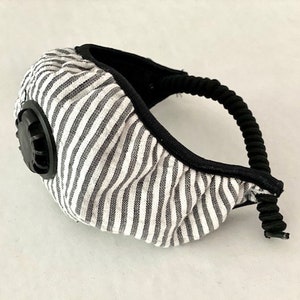 Può includere: Una maschera facciale a righe bianche e nere con una valvola nera. La maschera ha un elastico nero.