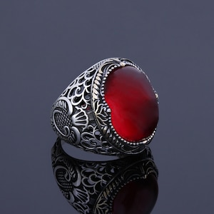 May include: A silver ring with an ornate design and a large, red gemstone.