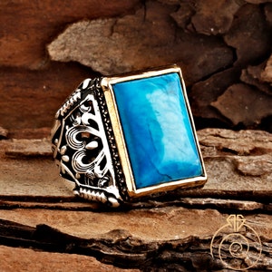May include: A silver ring with a blue turquoise stone set in a gold frame. The ring has an intricate design with a filigree pattern.