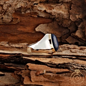 May include: A silver ring with a large, oval-shaped lapis lazuli gemstone. The ring is set on a wooden surface.