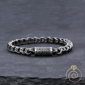 May include: A silver chain bracelet with a decorative, engraved clasp. The chain is made of interlocking links with a floral pattern.