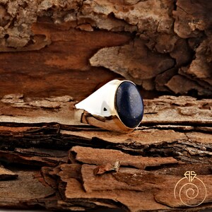 May include: A silver ring with a gold band and a large oval lapis lazuli gemstone. The ring is set against a brown wooden background.