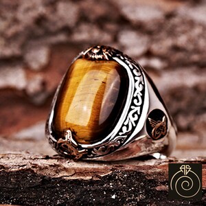 May include: A silver ring with an ornate design and a large oval-shaped tiger's eye gemstone.