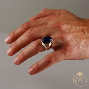 May include: A silver ring with a dark blue oval gemstone set in a gold bezel. The ring is on a person's finger.