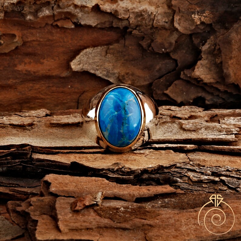 K&ouml;nnte beinhalten: Ein silberner Ring mit einem gro&szlig;en ovalen blauen Edelstein, der in der Mitte eingesetzt ist.