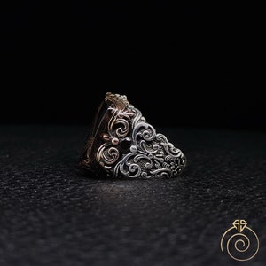 May include: A silver ring with a black stone and intricate floral designs. The ring is made of two-toned metal, with silver and rose gold accents.