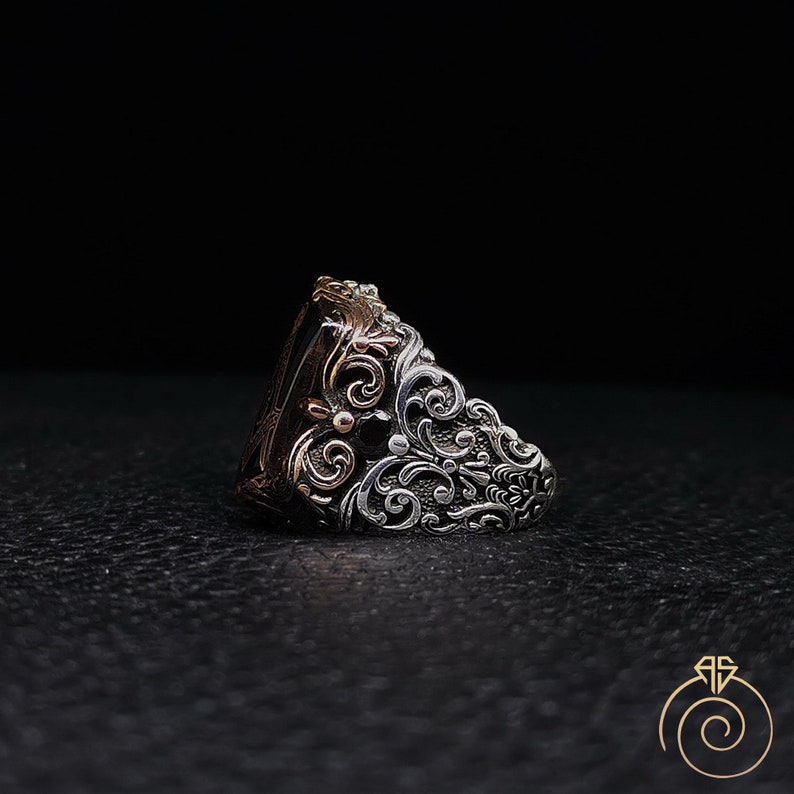 May include: A silver ring with a black stone and intricate floral designs. The ring is made of two-toned metal, with silver and rose gold accents.