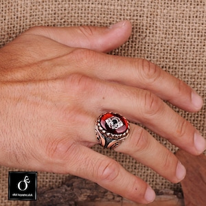 Pu&ograve; includere: Un anello d'argento con una pietra ovale rossa e dettagli in argento intricati. L'anello &egrave; su una mano.