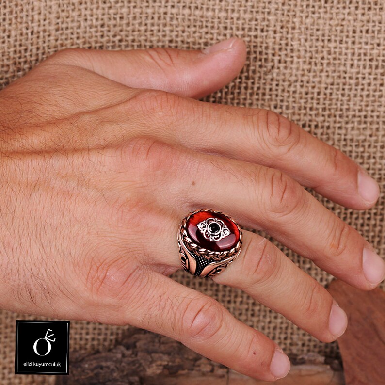 Pu&ograve; includere: Un anello d'argento con una pietra ovale rossa e dettagli in argento intricati. L'anello &egrave; su una mano.