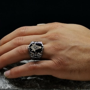 May include: A silver ring with a black onyx stone featuring a gold Masonic symbol.
