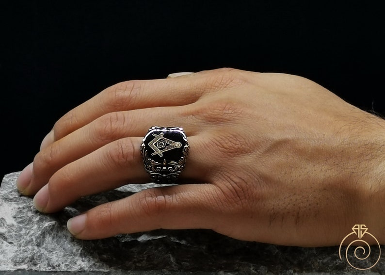 May include: A silver ring with a black onyx stone featuring a gold Masonic symbol.