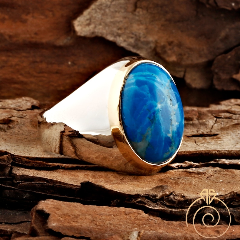 K&ouml;nnte beinhalten: Ein silberner Ring mit einer goldenen Einfassung und einem blauen ovalen Edelstein. Der Edelstein hat ein marmoriertes Muster.
