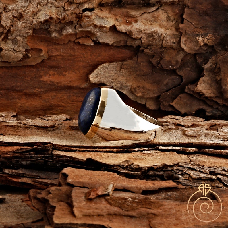 May include: A gold ring with a blue oval lapis lazuli gemstone. The ring is set on a wooden background.