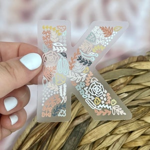 May include: A clear sticker with a floral design in shades of pink, yellow, and blue, forming the letter K.