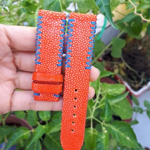 Può includere: Un cinturino per orologio in pelle arancione brillante con dettagli di cucitura blu. Il cinturino è realizzato in pelle di razza e ha una superficie testurizzata.