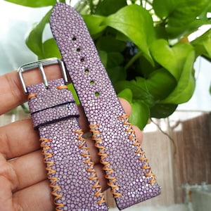 Può includere: Due cinturini per orologio in pelle viola con cuciture arancioni. I cinturini sono in pelle di razza e hanno una superficie testurizzata.