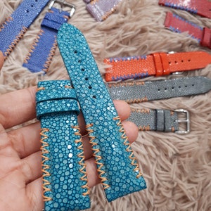 Può includere: Due cinturini per orologio in pelle blu turchese con cuciture arancioni. I cinturini sono realizzati in pelle di razza e hanno una superficie testurizzata.
