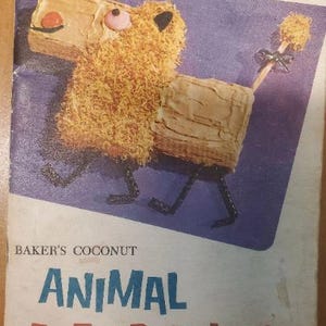 May include: A vintage book cover featuring a cartoon animal cake with a brown, yellow, and white frosting. The title of the book is "Baker's Coconut Animal Cut-Up Cakes".
