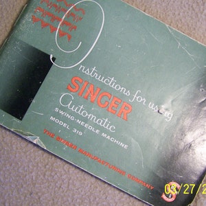 May include: Green instruction booklet for a Singer Automatic Swing-Needle Machine, Model 319. The booklet has the text "Instructions for using Singer Automatic Swing-Needle Machine Model 319 The Singer Manufacturing Company" printed on the front cover.