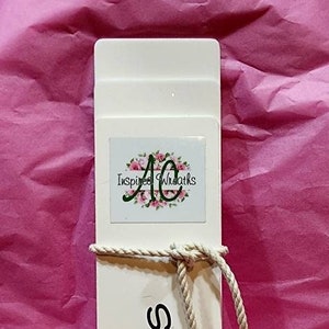 May include: White cardboard box with a white rope tied around it. The box has the text "Inspired Wreaths" and "FLEXI TAILS" printed on it.
