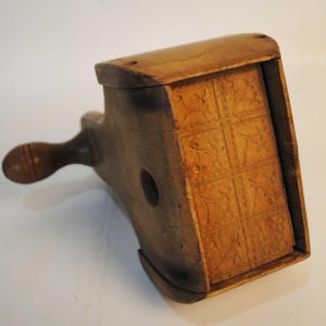 Peut inclure: Un moule à beurre en bois vintage avec une poignée et un motif floral décoratif sculpté dans la base. Le moule est en bois brun clair et de forme rectangulaire. La poignée est arrondie et fixée sur le côté du moule.