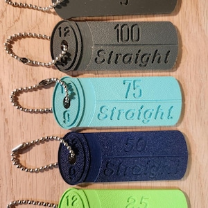 May include: Five keychains with different colored plastic tags. The tags have the words "Congrats", "100 Straight", "75 Straight", "50 Straight", and "25 Straight" printed on them.