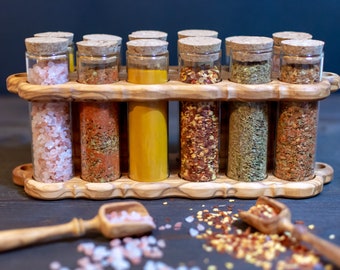 May include: A wooden spice rack with 10 glass jars filled with various spices, including pink Himalayan salt, red pepper flakes, turmeric, and dried herbs. The rack is made of olive wood and has a natural finish.