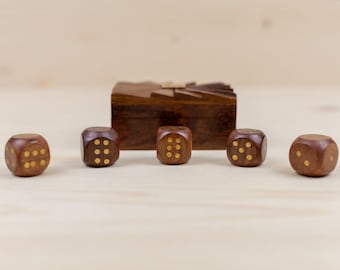 Könnte beinhalten: Ein Satz von fünf Holzspielwürfeln mit goldfarbenen Punkten, angeordnet vor einer kleinen Holzkiste. Die Würfel sind dunkelbraun, und die Punkte zeigen die Zahlen auf jeder Seite an. Die Kiste ist ebenfalls dunkelbraun.
