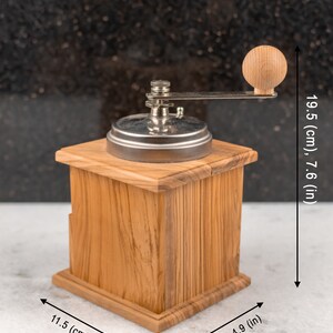May include: A wooden manual coffee grinder with a silver metal grinder and a wooden crank handle. The grinder is 7.6 inches tall, 4.5 inches wide, and 4.9 inches deep.