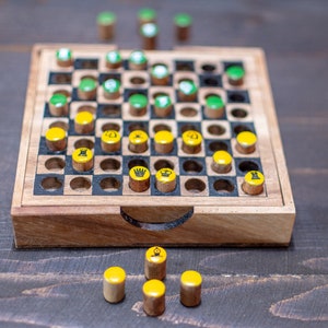 May include: A wooden travel chess set with a square playing board and cylindrical pieces. The pieces are yellow and green, with chess piece symbols. The board is set on a dark wooden surface.