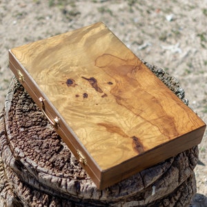 May include: A wooden box with a natural wood grain finish and brass accents. The box has a hinged lid and a handle on the top.