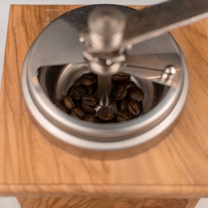 May include: A close-up of a wooden coffee grinder with a metal top. The grinder is filled with coffee beans.
