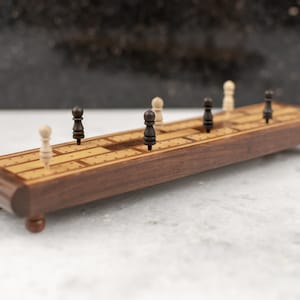 May include: A wooden game board with black and white pegs. The board is made of dark wood with a light wood inlay. The pegs are arranged in a line down the center of the board.