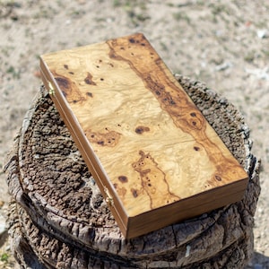 以下が含まれることがあります： 木目模様の天然木と真鍮製の蝶番が付いた木製の箱。箱は閉じており、木の切り株の上に置かれています。