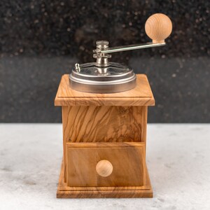 May include: A wooden coffee grinder with a metal top and a wooden handle. The grinder has a drawer on the front and a knob on the side.