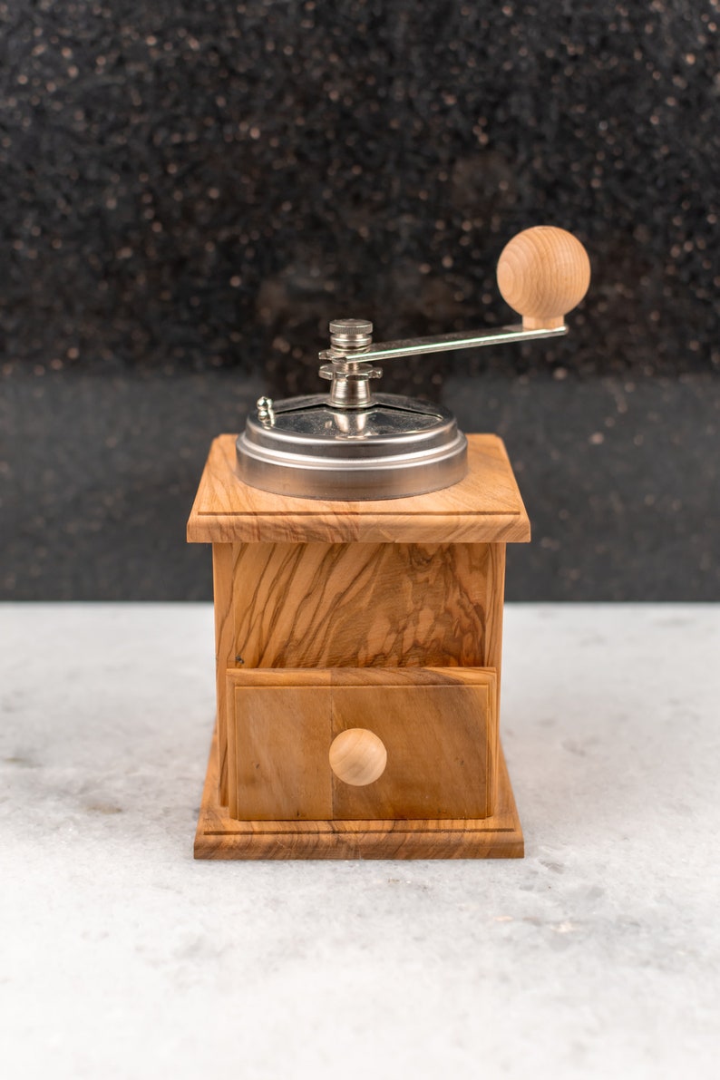 May include: A wooden coffee grinder with a metal top and a wooden handle. The grinder has a drawer on the front and a knob on the side.