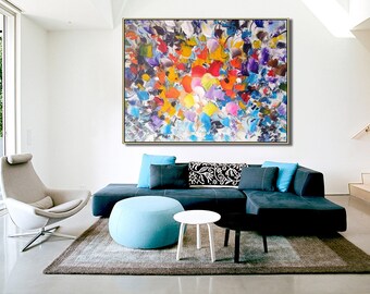May include: Abstract painting with a colorful, textured design featuring shades of blue, red, yellow, purple, and white. The painting is framed and hanging on a white wall in a living room setting.