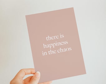 May include: A light pink card with the text "there is happiness in the chaos" printed in white.