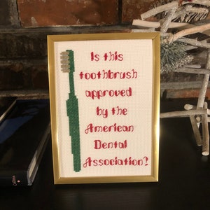 May include: A framed cross-stitch design with a green toothbrush and red text that reads "Is this toothbrush approved by the American Dental Association?"