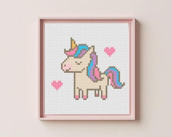 Puede incluir: Un punto de cruz enmarcado de un unicornio con cuerpo color crema, cuerno dorado y melena y cola coloridas. Dos corazones rosas flanquean el unicornio. El marco es de color rosa claro.