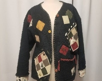 May include: A dark teal, textured cardigan with colorful patchwork details. The jacket features a V-neck, button closure, and decorative stitching. Patches include squares and rectangles in shades of yellow, red, and green. The cuffs have a patterned fabric.