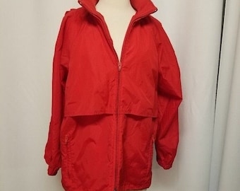 May include: A bright red jacket with a high collar and a full-length zipper. The jacket has long sleeves, a drawstring at the bottom, and a small pocket on the left side. The jacket is displayed on a mannequin.