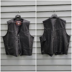 May include: A black leather vest with a button-up front, two front pockets, and a notched collar. The vest is hanging on a black hanger against a grey wooden background. The back of the vest is also shown.