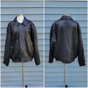 May include: A black leather jacket displayed on a mannequin, shown from the front and back. The jacket has a collared neckline, a zipper closure, and two front pockets. The jacket is a classic style.