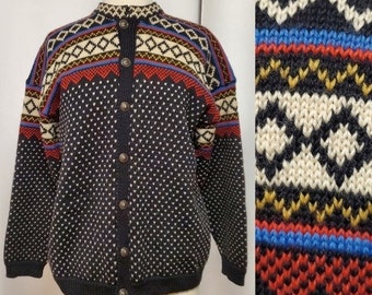 Könnte beinhalten: Dunkelblauer Cardigan mit Knopfleiste und detailliertem geometrischen Muster in Rot, Weiß und Blau. Der Pullover hat einen runden Ausschnitt und lange Ärmel. Das Muster wiederholt sich auf der rechten Seite des Bildes.