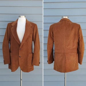 May include: A brown corduroy blazer with a two-button closure, front pockets, and a chest pocket. The jacket is displayed on a mannequin, showcasing the front and back views. The blazer has a classic lapel and buttoned cuffs.